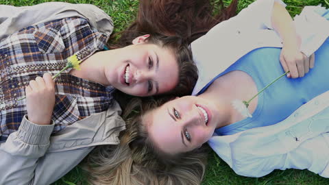 Women Smiling and Relaxing on Grass with Flowers in Park