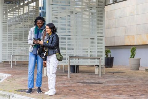 Young couple checking smartphones and holding bicycle helmet in modern urban plaza