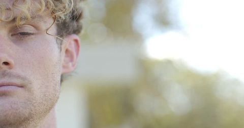 Sunlit close-up portrait standing young man with curly blond hair and stubble, calm headshot