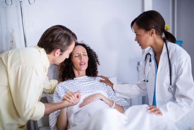 Doctor and man comforting pregnant woman in ward of hospital