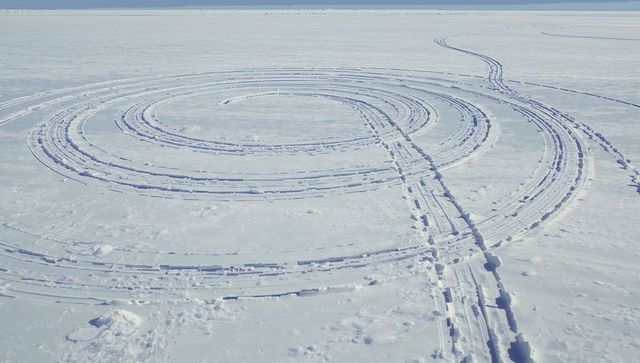Concentric snow tracks carving rings on frozen lake, segmented ruts and ice blocks