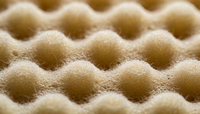 Macro beige egg-crate foam texture showing porous fibrous repeating ridges and soft shadows