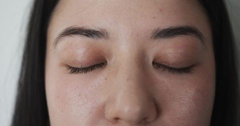 Asian woman resting with closed eyes showing natural skin texture and groomed eyebrows