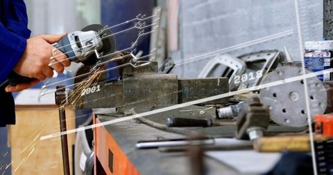 Worker hands grinding metal with angle grinder in industrial workshop, sparks and fabrication