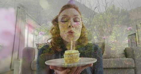 Woman Blowing Cupcake Candle with Floral Double Exposure in Cozy Living Room