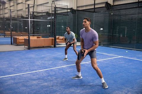 Men playing padel doubles on indoor blue court preparing for return and serve