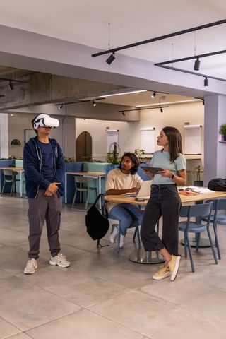 Coworkers testing virtual reality demo in modern coworking space with laptop and tablet