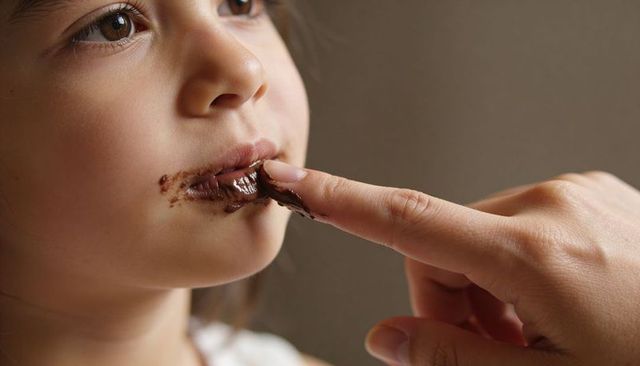 Caregiver cleaning chocolate from child's lips with finger intimate closeup family bonding