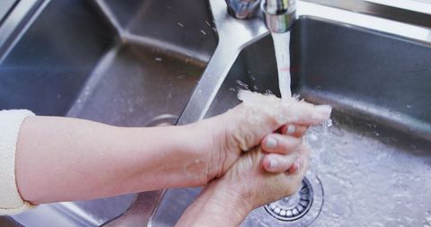 Senior woman washing hands in kitchen sink for hygiene