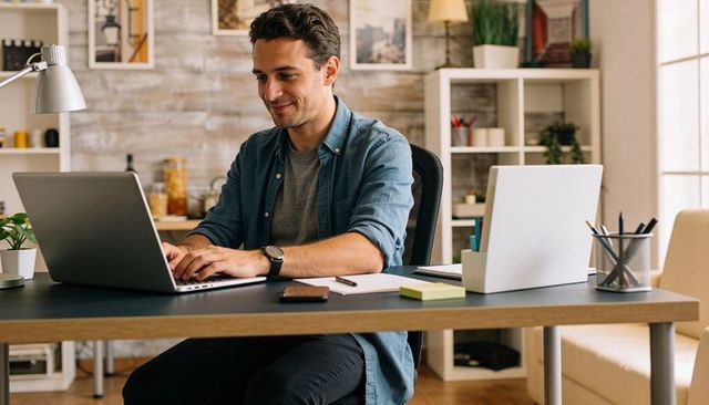 Young man working on laptop in modern home office with organized desk and natural light