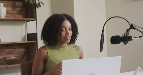 African american woman recording podcast from home studio using laptop and microphone