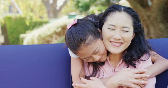A mother and daughter embrace joyfully outdoors in a sunlit garden. The mother is smiling blissfully, conveying a sense of love and affection. This imagery is ideal for promoting family values, parenting blogs, Mother's Day campaigns, or advertisements focusing on family relationships and happiness.
