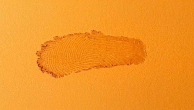 Glossy fingerprint impression on orange textured paper with liquid beads macro closeup