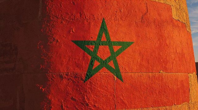 Weathered moroccan flag painted on textured red masonry wall with green pentagram