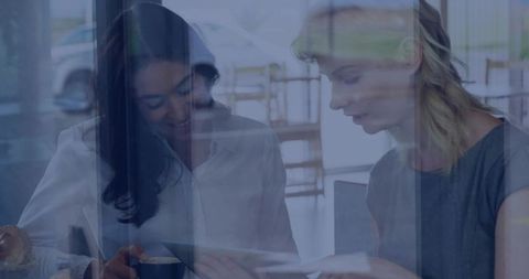 Two Professional Women Collaborating Over Tablet in Bright Office with Glass Reflections