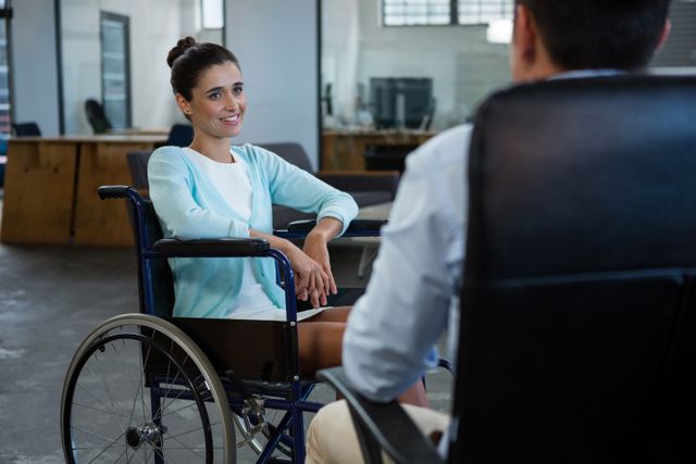 Businesswoman in wheelchair engaging in conversation with colleague in modern office. Ideal for illustrating workplace diversity, inclusion, and professional interactions. Suitable for corporate websites, diversity and inclusion campaigns, and business communication materials.
