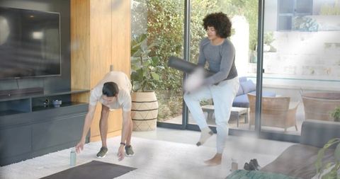 Home workout duo using foam roller, floor mat, water bottle in bright living room with patio