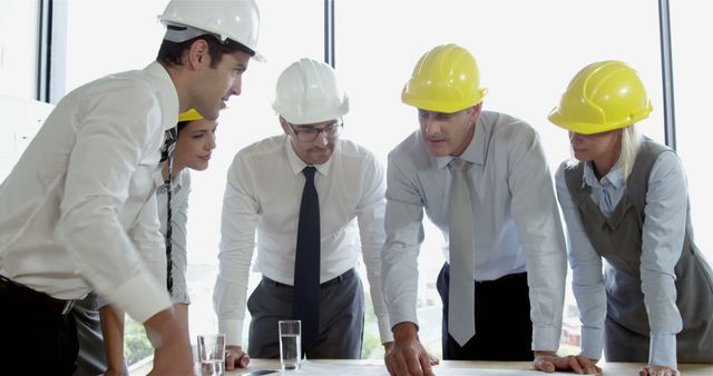 A diverse group of professionals, in the construction or engineering field, are engaged in a discussion over plans, with copy space. They are focused and collaborating, indicating teamwork and problem-solving in a business context.