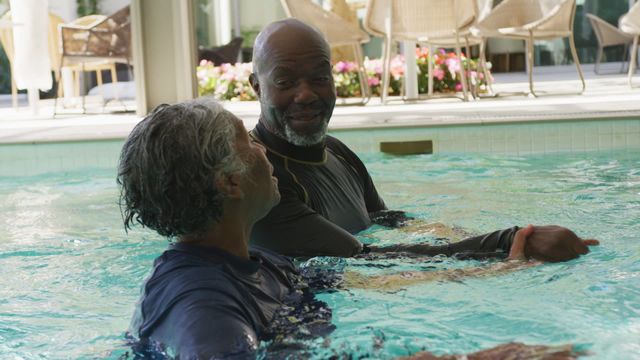 Two smiling individuals enjoying a refreshing swim in a pool, representing the joys of an active retirement lifestyle. Perfect for use in brochures, articles about healthy living for seniors, or promotional materials for retirement communities.