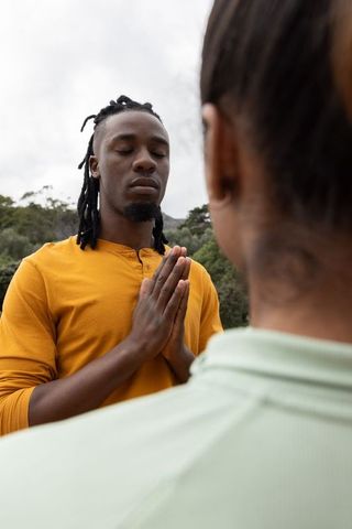 Couple practicing mindful meditation outdoors facing wooded hills during breathwork