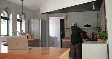 Indian man preparing coffee on stove in rustic minimalist kitchen with laptop on island