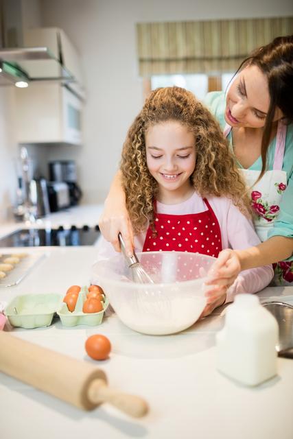 Mother and daughter engaging in a fun baking activity at home. Suitable for concepts of family bonding, parenting, home cooking, and domestic life. Ideal for use in ads or articles related to family life, culinary arts, and wholesome activities.