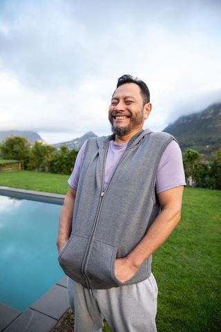 Smiling asian man standing by pool in grey sleeveless hoodie and purple tee
