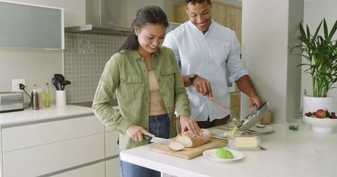 Diverse couple cooking on modern kitchen island, slicing bread and tipping scrambled eggs