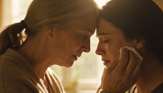 Mother comforting adult daughter wiping tears closeup warm backlit intimate moment