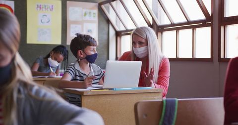 Teacher helping student with homework on laptop in classroom