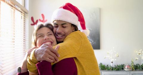 Diverse couple sharing warm christmas hug wearing santa hat and cozy sweaters