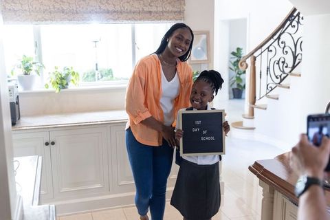 African american mom and daughter posing for first day of school with letter board at home