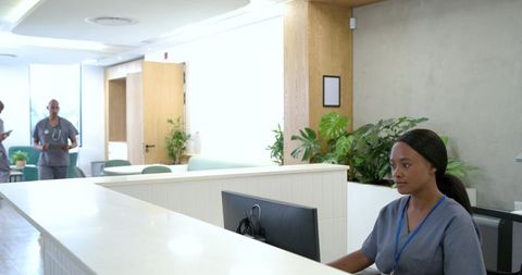 Medical receptionist assisting patients at modern clinic front desk with computer