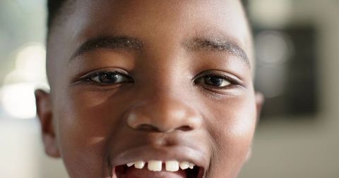 Closeup smiling african american boy showing missing front teeth at home window soft light