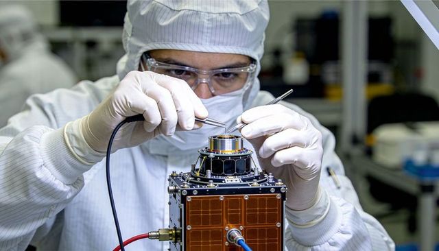 Cleanroom technician assembling and inspecting cubesat with precision tools in laboratory