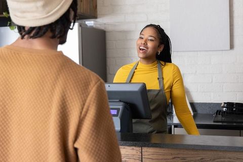 Friendly african american barista serving customer at cozy cafe counter with pos