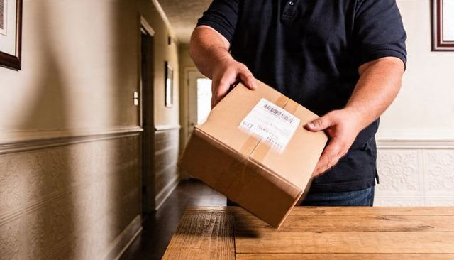 Courier placing cardboard parcel on wooden table in sunlit hallway with visible barcode