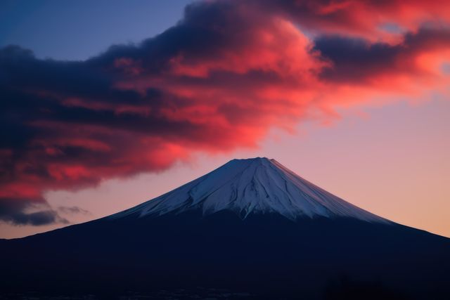 Red clouds hovering over the snow-capped peak of Mount Fuji at sunset create a dramatic and breathtaking scene. This beautiful nature landscape showcases the iconic mountain in Japan, perfect for travel websites, nature blogs, postcards, and promoting outdoor activities.