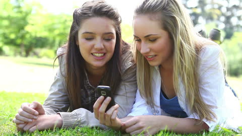 Happy Friends Relaxing on Grass While Using Smartphone