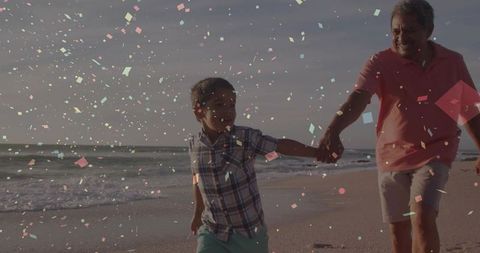 Grandfather and grandson walking hand in hand on sunlit beach with confetti overlay