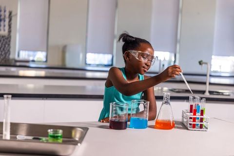 Young black girl wearing safety goggles conducting colorful chemistry experiment in lab