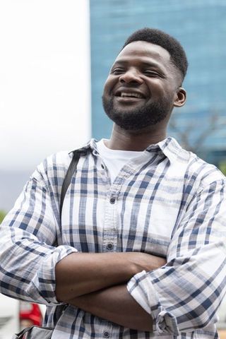 Confident african american man standing with arms crossed smiling on modern urban plaza
