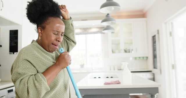 Woman singing into mop handle while cleaning kitchen - Download Free Stock Images Pikwizard.com