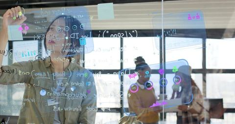 Women Collaborating on Glass Board with Digital Charts and Tablet in Modern Office