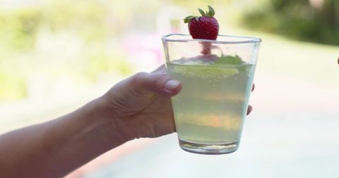 Hand holding chilled lime drink garnished with strawberry at poolside summer refreshment