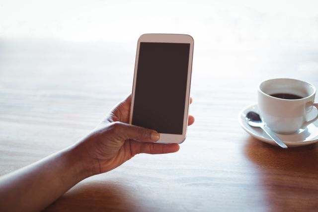Woman holding smartphone with blank screen while having coffee in a restaurant. Ideal for illustrating concepts of technology use, digital communication, modern lifestyle, and casual dining. Perfect for blogs, advertisements, and articles related to mobile technology, coffee culture, and everyday life.