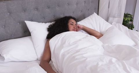 African woman sleeping peacefully under white duvet against tufted gray headboard