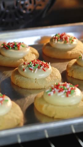 Vertical video placing tray of iced sugar cookies with festive sprinkles into oven