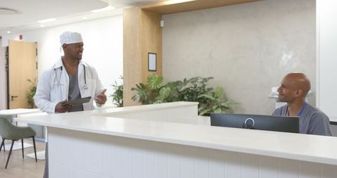 Smiling medical staff collaborating at modern clinic reception desk with tablet and pc