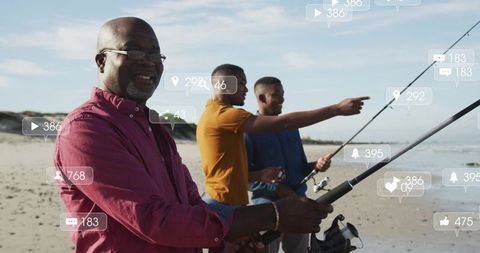 Smiling senior man fishing with friends on sandy beach with social media notifications